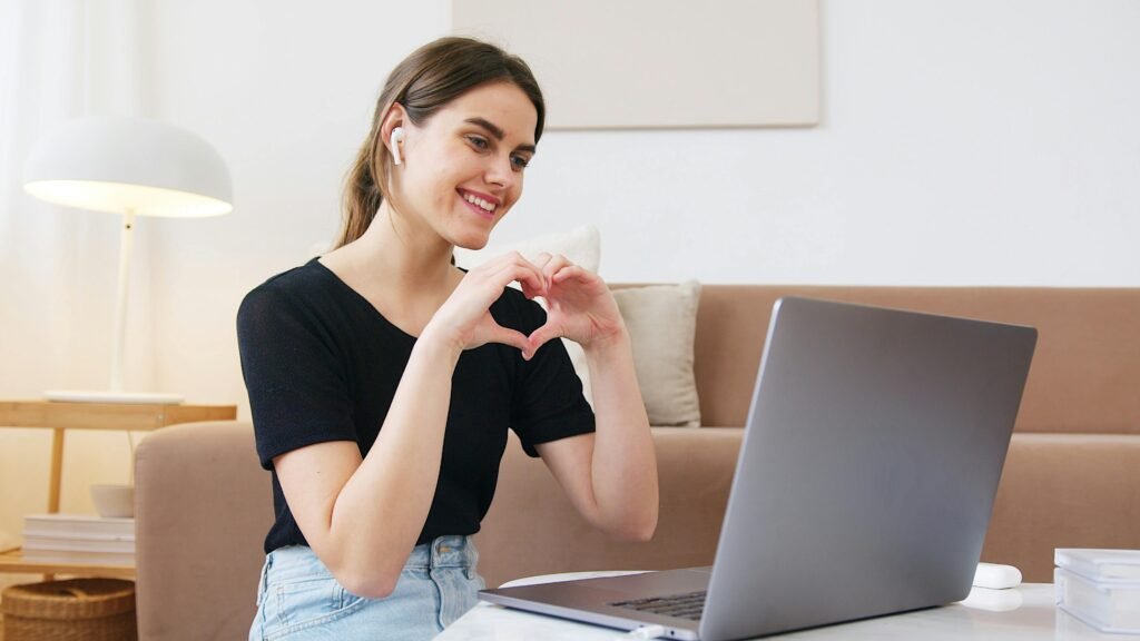 pexels-photo-4492134-4492134 Cheerful happy young female in jeans and black shirt having conversation via video call on laptop and making heart shape with fingers while sitting on floor in modern living room